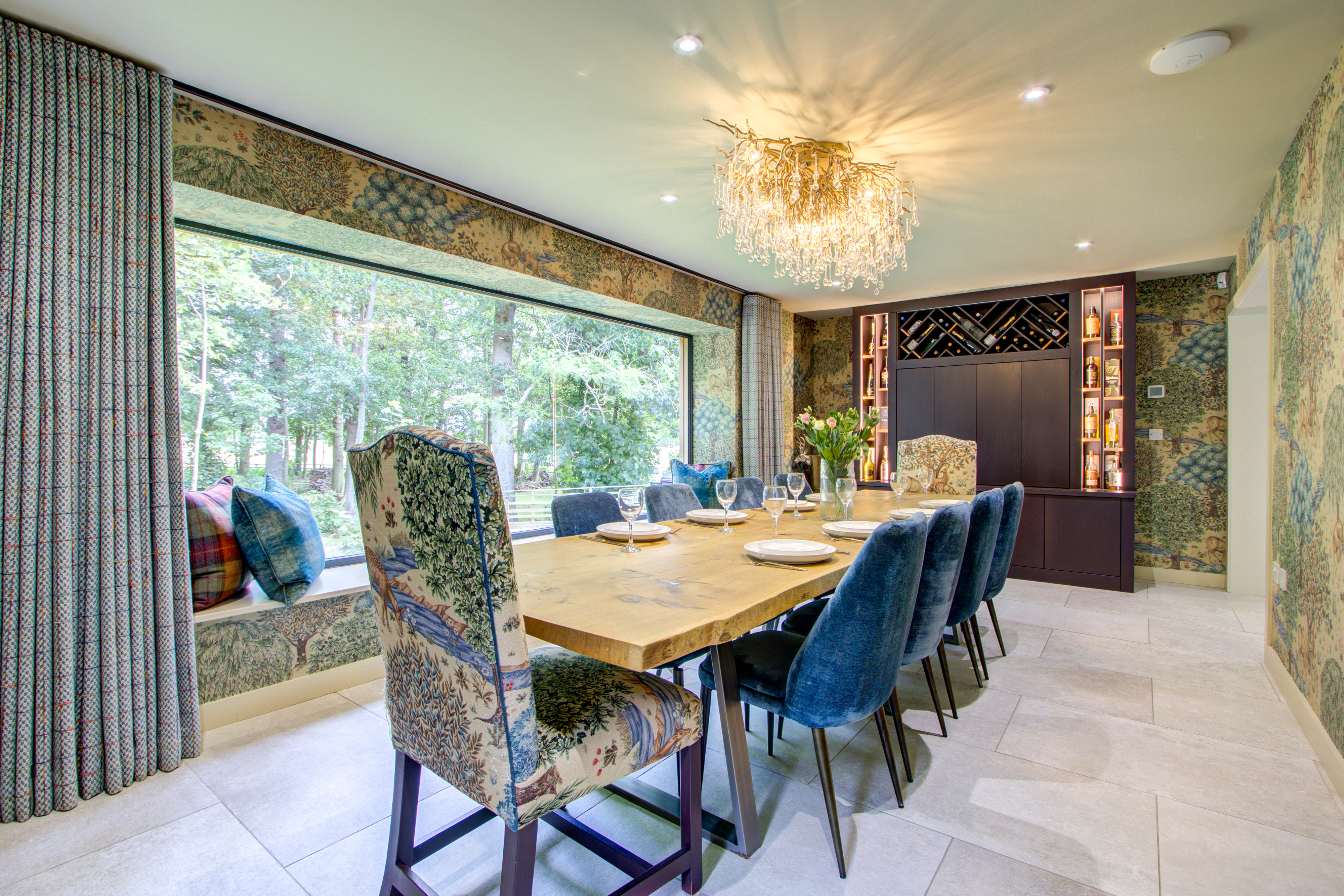 High Beeches dining room with a chandelier, blue upholstered chairs and a large woodland-facing window.
